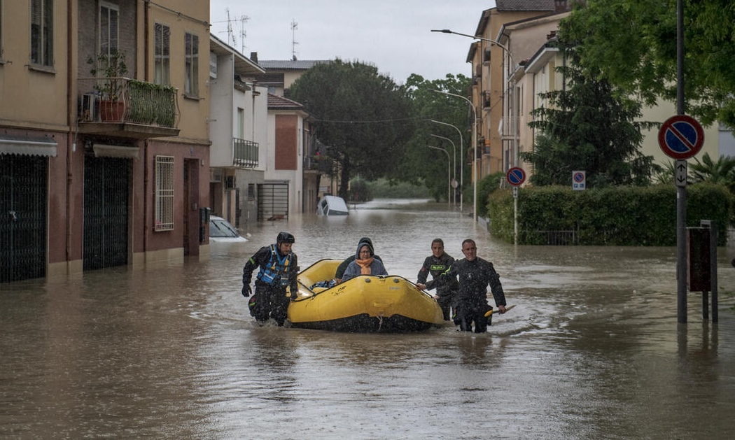 Soccorritori trasportano una persona su un gommone lungo una strada allagata in Emilia-Romagna, dove le gravi alluvioni hanno sommerso abitazioni e automobili.